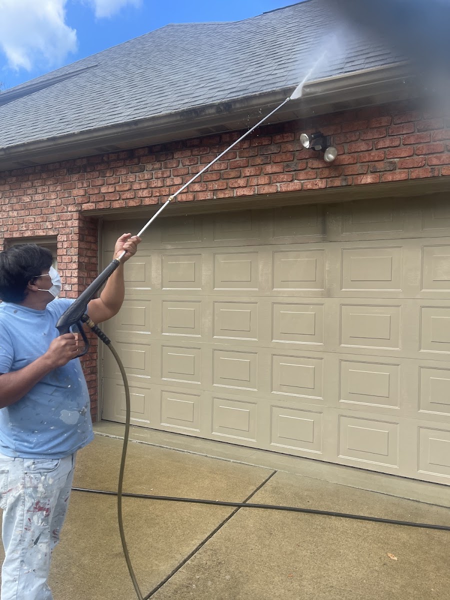 Minhas power-washing a brick garage and roofline before painting